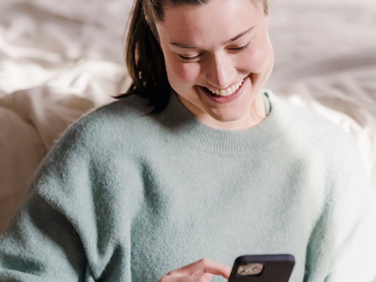 A guest smiling at her phone while messaging on the bed