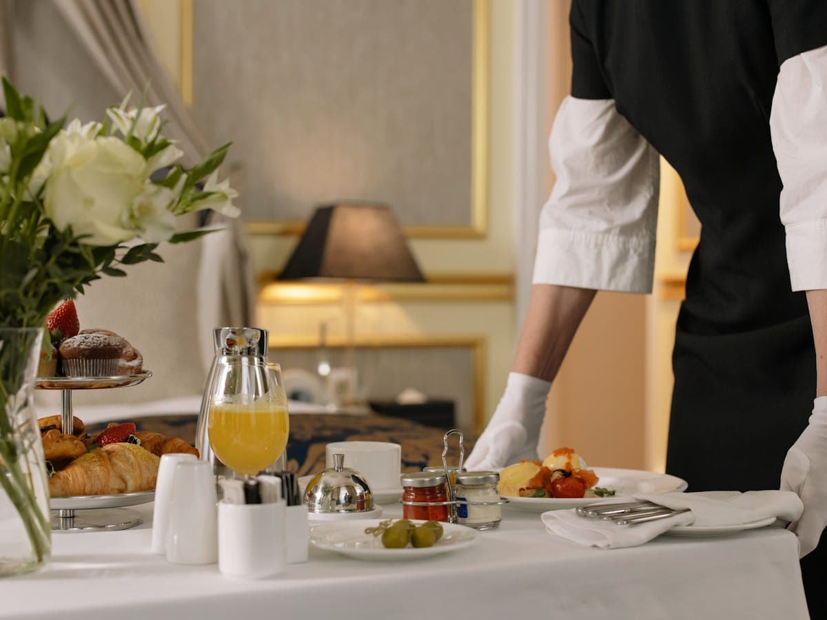 A butler setting down a luxury hotel breakfast tray with pastries and orange juice